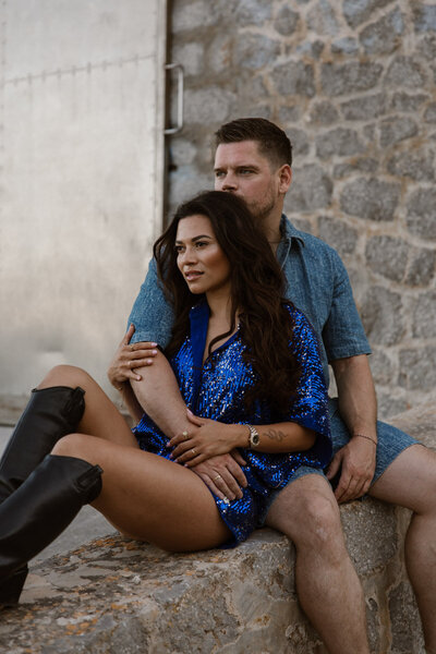 A man and woman are sitting against each other on a wall for a couple shoot.