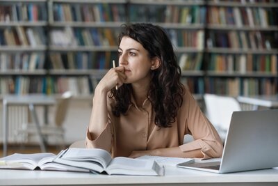 Young woman in a brown shirt looking thoughtfully to the side as she studies for her PA Exams