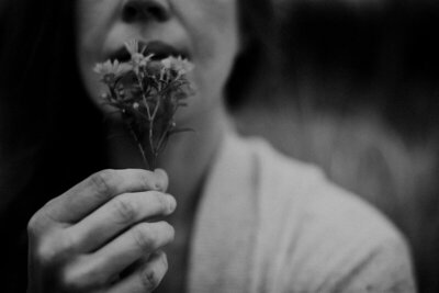 Black and white photo of a woman holding small flowers by her nose