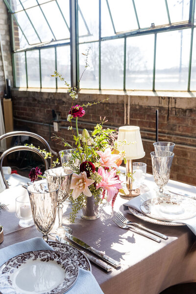Centerpiece and Tablescape from a Wedding Styled Shoot in Atlanta. Tablecloth is mauve, with floral printed plates, and a light pink, fuschia, and greenery centerpiece