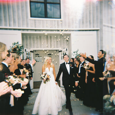 Bride and groom leaving ceremony holding hands while bridal party cheers and throws petals around them