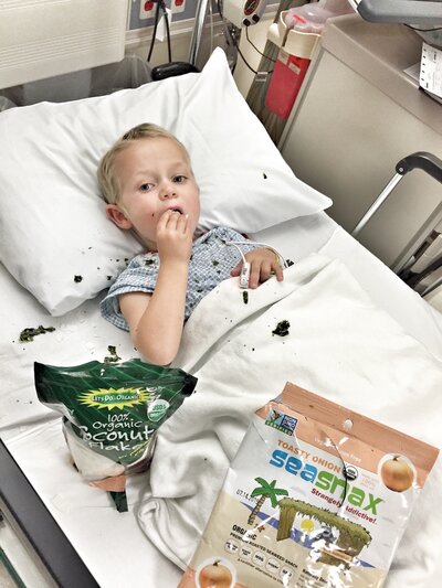 Little boy laying in a hospital bed eating snacks