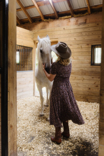Woman standing with her horse in a barn doorway, offering calm presence and equine-facilitated support