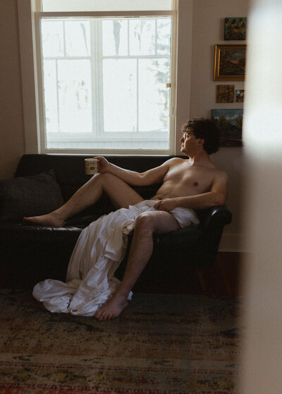 boudoir portrait of a man sitting on a couch under a window