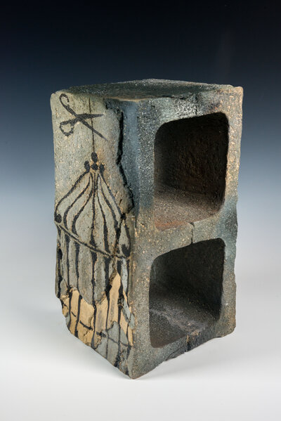 A cinder block that was hand made out of clay is decorated with underglaze to resemble graffiti and various other imagery