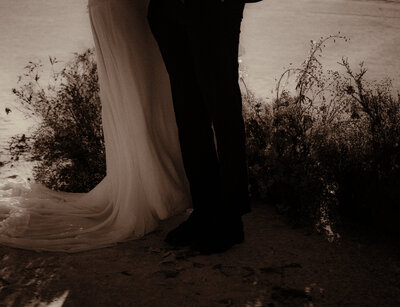 Bride and grooms legs stand in front of flowers in the sunset at Bonneville Salt Flats.