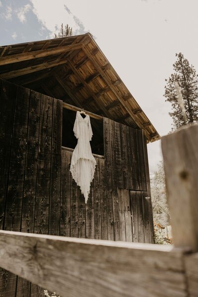 Boho-style wedding dress hanging on a rustic barn door before an intimate North Idaho wedding.