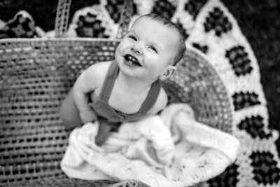Black and white photo of a baby inside a basket. The baby is on his knees looking up at the sky and smiling