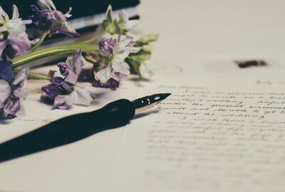 Handwritten letter with black calligraphy pen and purple flowers sitting on the letter.
