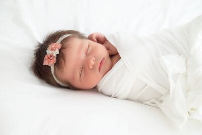 Baby girl sleeping in white and pink floral headbandand white swaddle during Newborn Photography Session in Alpharetta.