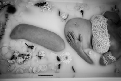 Black and white photo of a pregnant woman in a bathtub with flower petals