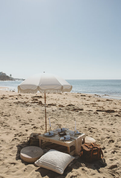 Let's Picnic Co. - Picnic table and umbrella with blue pillows and decor in Cornona Del Mar California