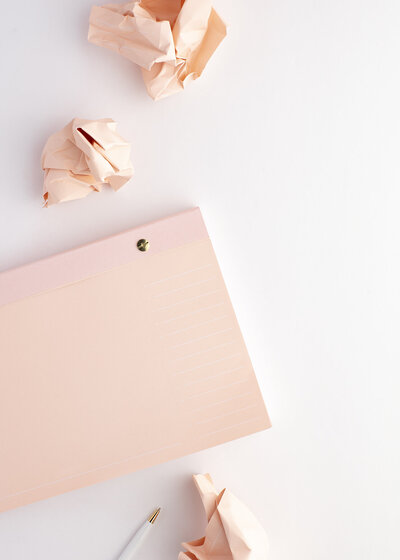 Pink notebook laying next to crumpled pieces of paper