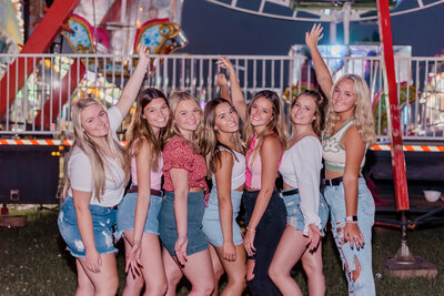 Rachel B Photography's Senior Rep Team poses together for the camera with their arms in the air in front of a carnival ride.