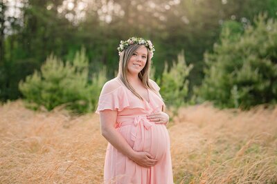 Expectant  mother holding her belly in soft pink dress and wearing floral crown
