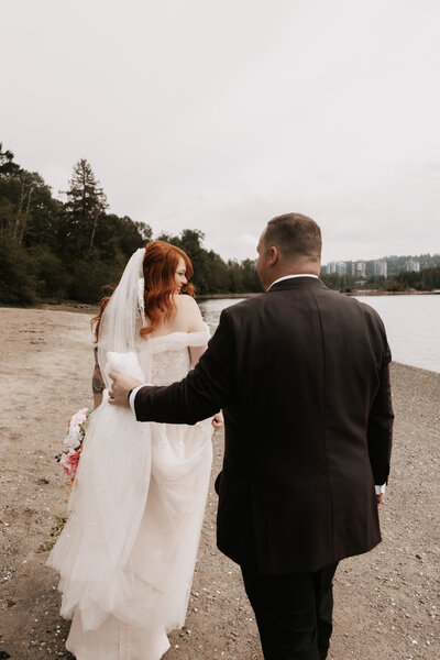 Bride and groom walk on a lake shore in Vancouver