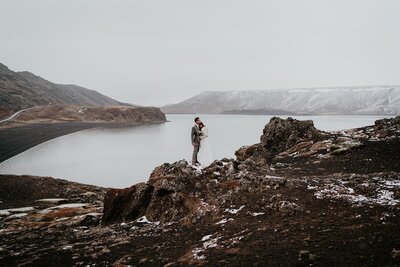 Bride and groom hug on a snowy, rocky trail surrounded by water during their Iceland elopement. 