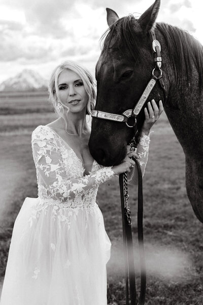 bride standing outside next to a horse while holding it's face with mountains in the background