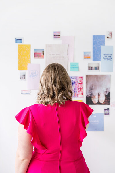 Photo of Kat Murphy from the back arranging photos and papers in a collage on the wall