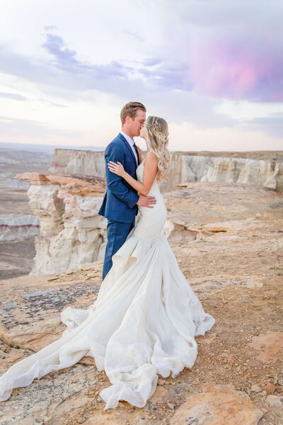 A bride and groom stand on the edge of the grand canyon kissing.