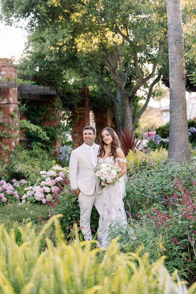 A groom leaning on a wall with his partner standing next to him