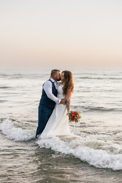 A groom on a snowboard in a blue suit embraces a bride on skis with Mt. Hood in the background at this Oregon ski elopement.