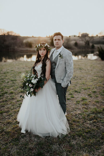 Bride and Groom standing in front of pond looking at camera during their wedding day