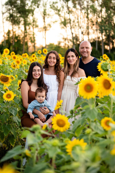 Mom and dad with their teenage daughters and toddler son in a sunflower field at the golden hour for their summer outdoor family photography session in Burlington, Ontario 