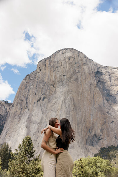 Intimate moment as two women embrace in Yosemite Valley, with El Capitan towering behind them during their engagement session