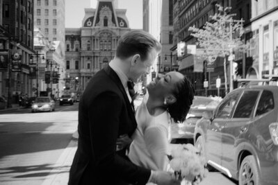 A couple embraces and laughs on their wedding day in front of city hall in Philadelphia