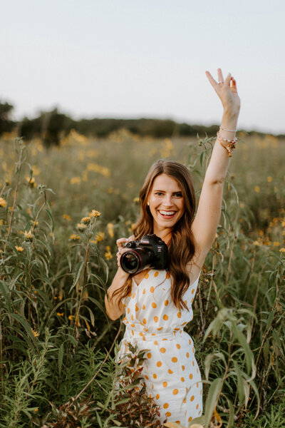 Jenna holding her camera holding up a peace  sign and smiling at the camera