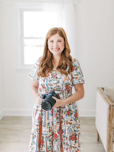 A photographer standing in her indoor studio holding her camera.