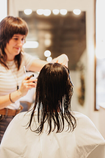 The back of a client's head with a hairdresser out of focus in the background at a Eugene hair salon.