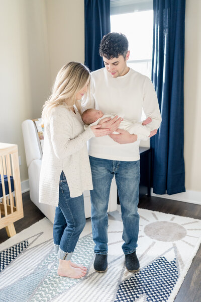 New parents hold their newborn baby in his nursery at home.