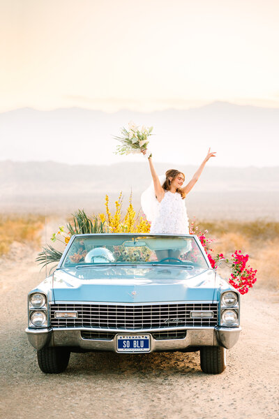 woman standing in vintage convertible with bouquet