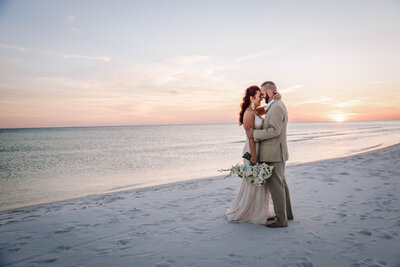 Newlyweds holding each other at Sunset on the white sand beach of Destin, FL.