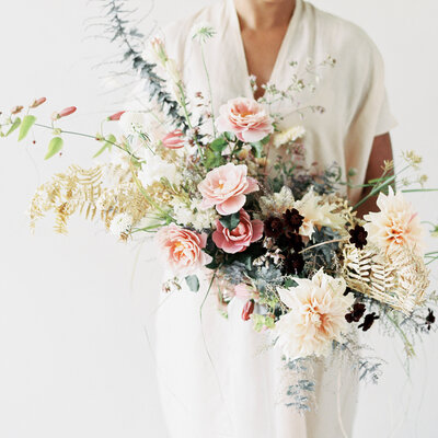 A bride holds a large asymmetrical garden bouquet at a Montreal studio.