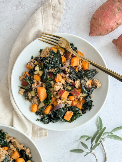 A bowl of ground turkey, kale and sweet potato with red onions and fresh sage leaves on the side.