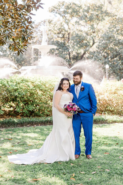 Close-up of a bride holding a vibrant bouquet with pink peonies, peach roses, and blue accents, tied with a light blue ribbon during a Savannah elopement.