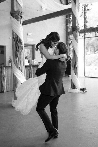 Black and white photo of a groom lifting his bride in celebration during a joyful Austin wedding reception planned with heart.