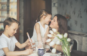 Daughter and mother rubbing noses while sibling draws off to the side.