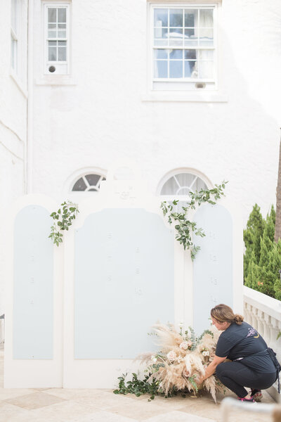 Behind-the-scenes moment of planner styling floral décor on a wedding seating chart, highlighting design services by The Eventful Gals.