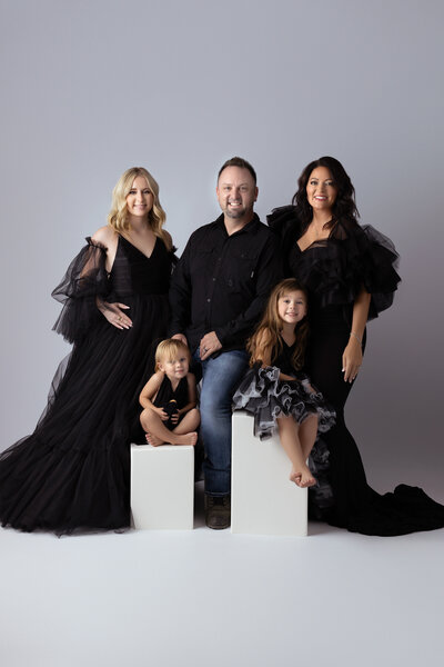 A beautiful family dressed in elegant black gowns and outfits, captured by a Dallas family photographer, showcasing their timeless style in a studio setting.