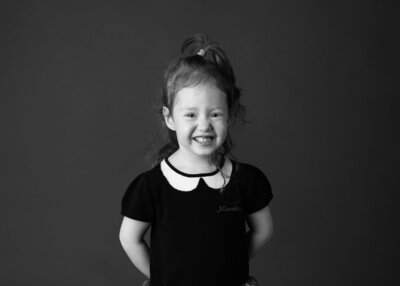 A young girl smiling proudly on his first day of school photo in black and white.