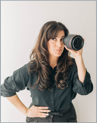 photo of a woman smiling at the camera while holding a camera in her right hand