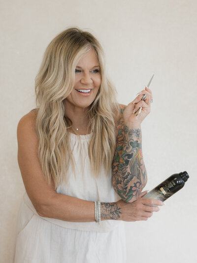 hair stylist with blond hair holding cutting sheers and hair spray