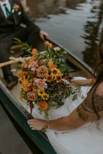 bride holds fall wedding bouquet while sitting in canoe