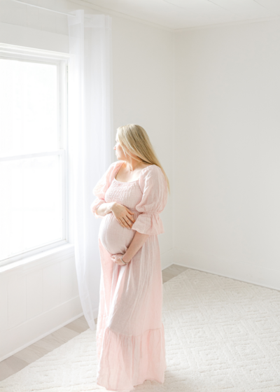 pregnant woman holds baby bump and smiles during boston maternity photoshoot