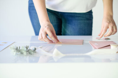 personal branding photos of a stationary designer arranging an invitation on a white desk with the reflection of the paper in the desk