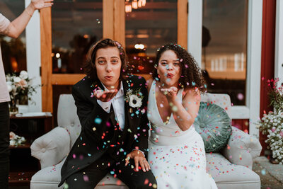Newlywed couple blowing confetti toward the camera